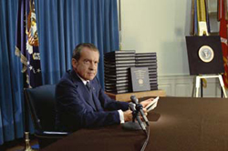 Nixon sitting at table.  Behind him, transcripts of Watergate tapes are on display